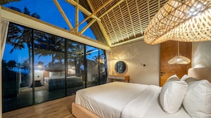 A modern bedroom with a large bed, a wooden floor, and a view of palm trees through floor-to-ceiling windows. - Green Harmony Villas (Gianyar)