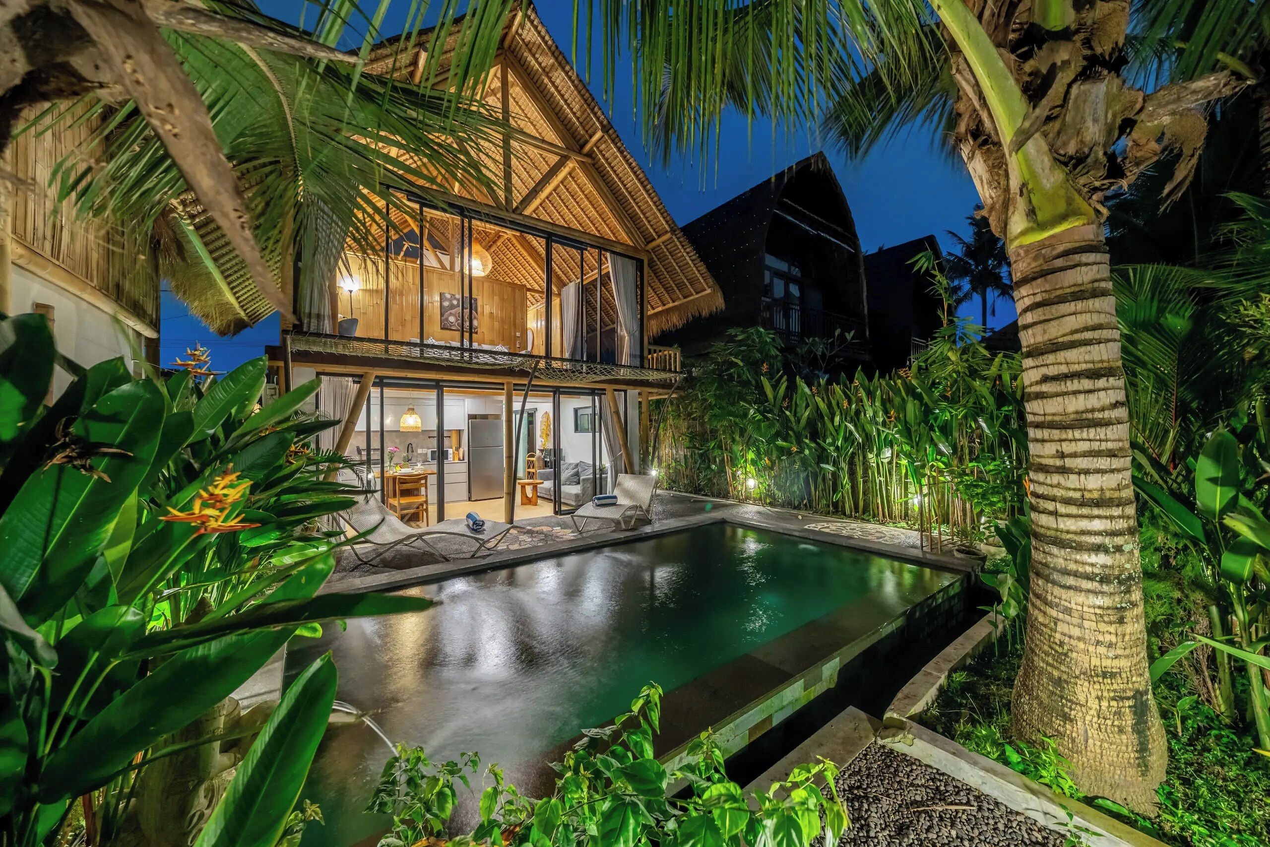 A two-story house with a swimming pool, surrounded by tropical vegetation.