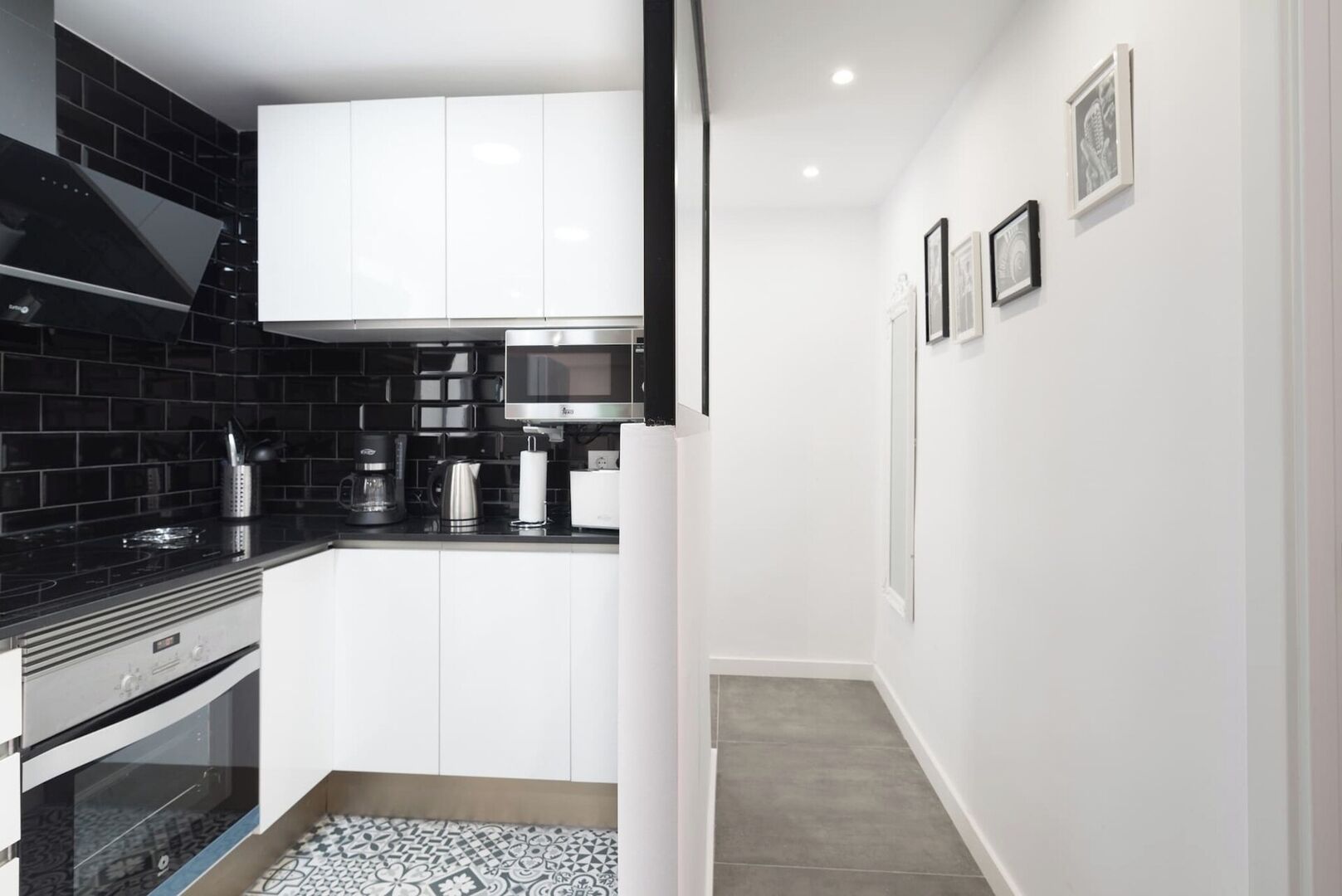 A modern kitchen with white cabinetry, a black backsplash, and a stainless steel range hood.
