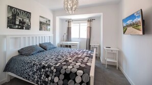 Ein Schlafzimmer mit Bett, Schreibtisch, Stuhl, Fernseher und Kunstwerken an den Wänden.