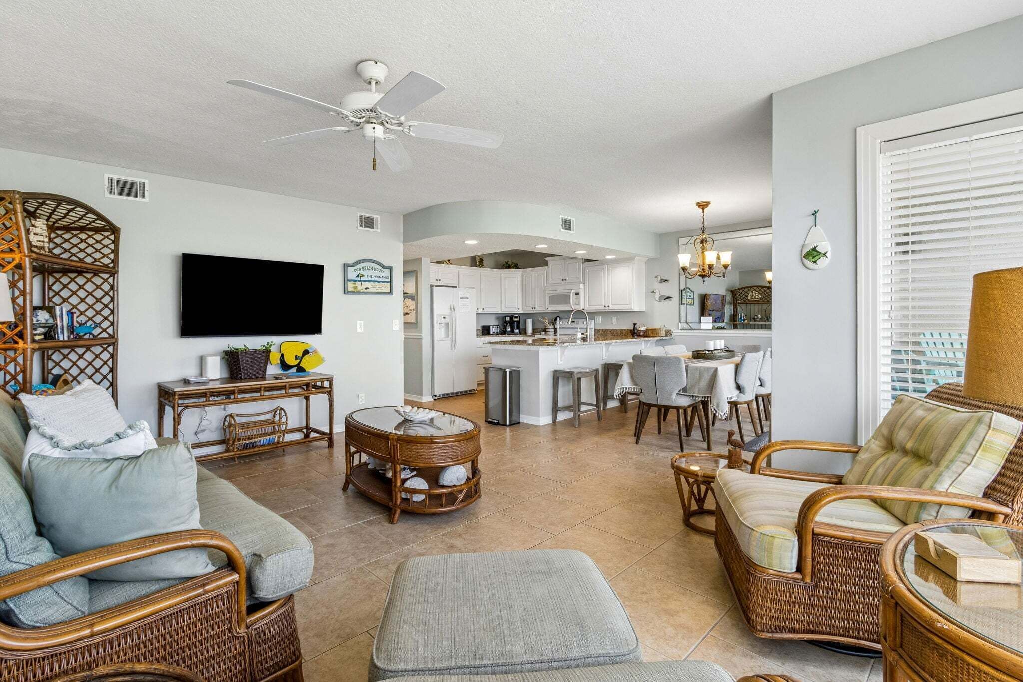 Amplia sala de estar con una televisión de pantalla plana grande, muebles de mimbre, una mesa de comedor con sillas y una cocina al fondo.