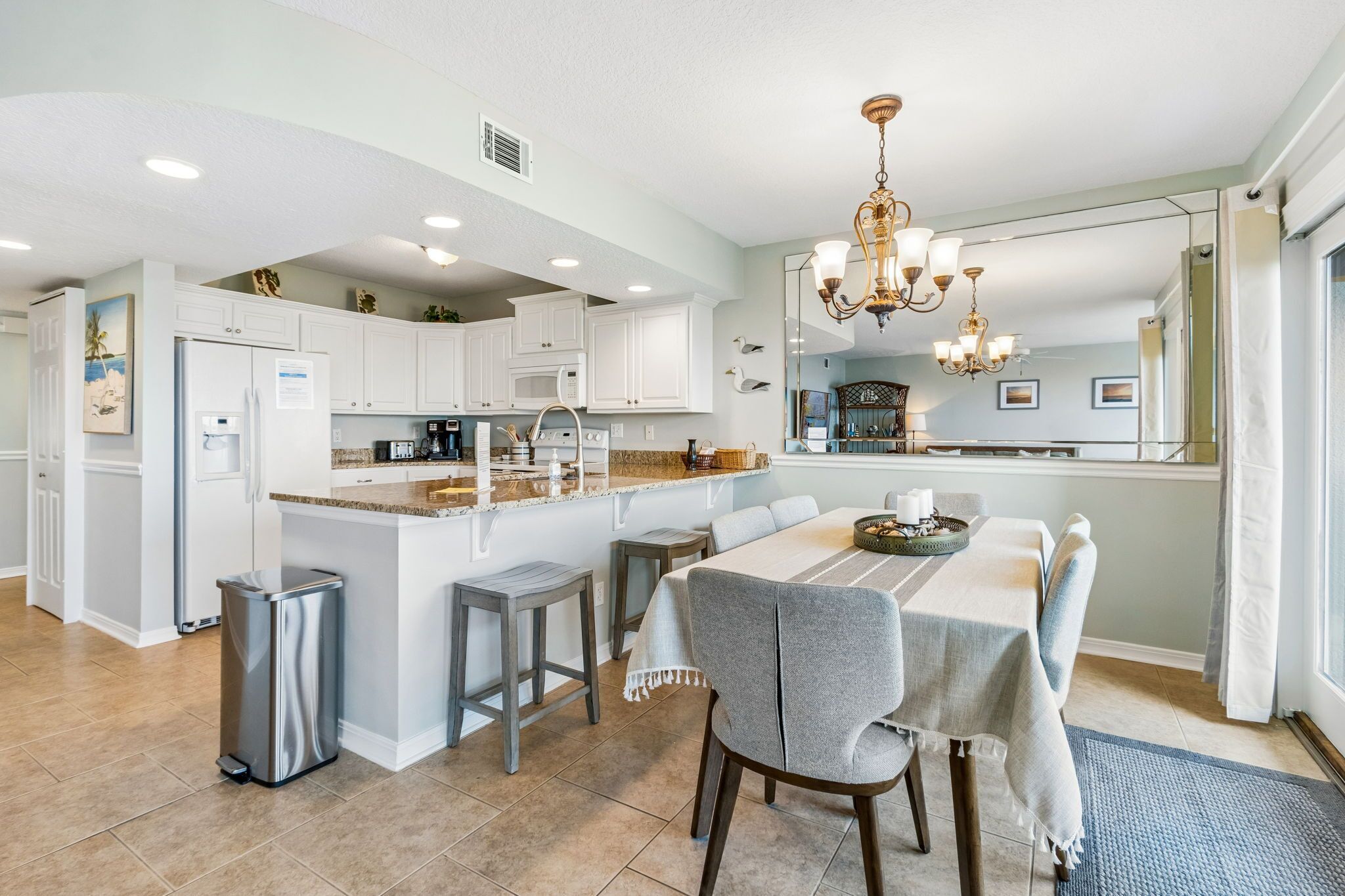 A modern kitchen with white cabinetry, a central island, and a dining area with a chandelier.