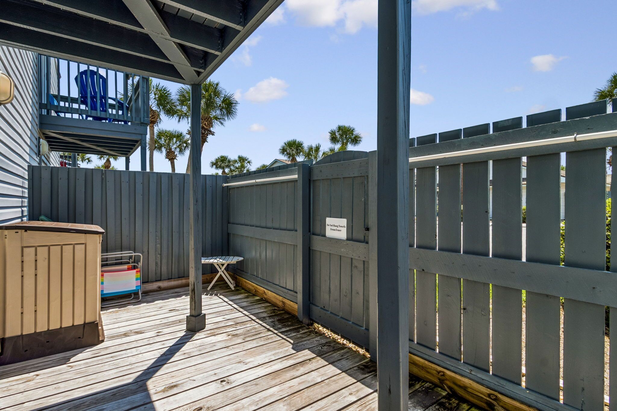 A wooden deck with a table and chairs, a hot tub, and a fenced area with a sign.