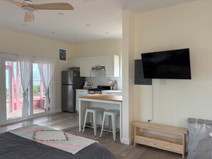 A compact kitchen with a refrigerator, stove, and a flat-screen TV mounted on the wall.