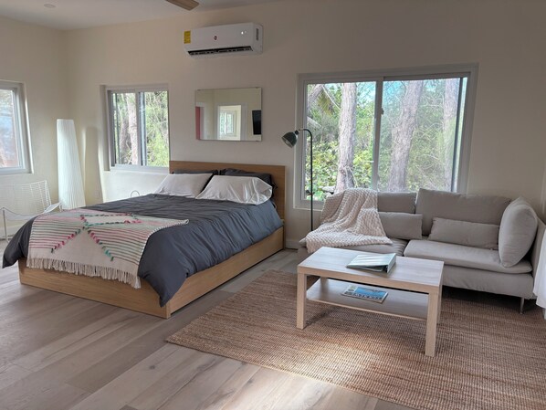 A bedroom with a bed, a sofa, a coffee table, and large windows.