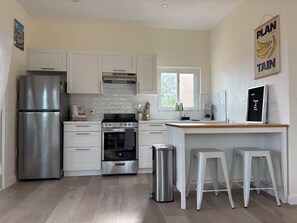 A modern kitchen with white cabinets, stainless steel appliances, a window, and a 'Plan Tain' sign.