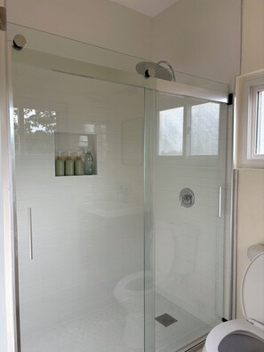 A modern bathroom with a glass-enclosed shower, a toilet, and a shelf with toiletries.