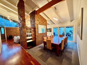 Un'ampia sala da pranzo con una parete decorata in mattoni, un grande tavolo di legno e vista all'esterno tramite una porta scorrevole in vetro.