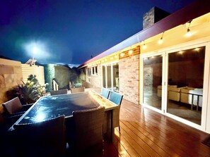 Patio esterno con tavolo e sedie, un muro in mattoni e una porta vetrata che dà su un ambiente interno.