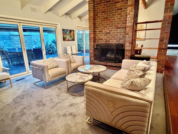 A living room with a fireplace, two sofas, a coffee table, and a large sliding glass door leading to an outdoor area.