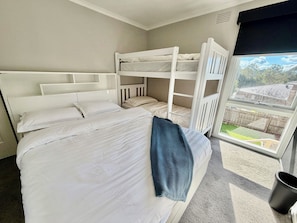 A room with bunk beds, a window with a view of a backyard, and a black trash bin.