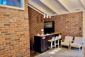 A modern bar area with a brick wall, a black counter, and white bar stools.