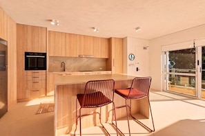 A modern kitchen with wooden cabinets, a built-in oven, and a large window. - Picture Point Penthouse 12 - Renovated Coastal Retreat with Sunset Views (Noosa)
