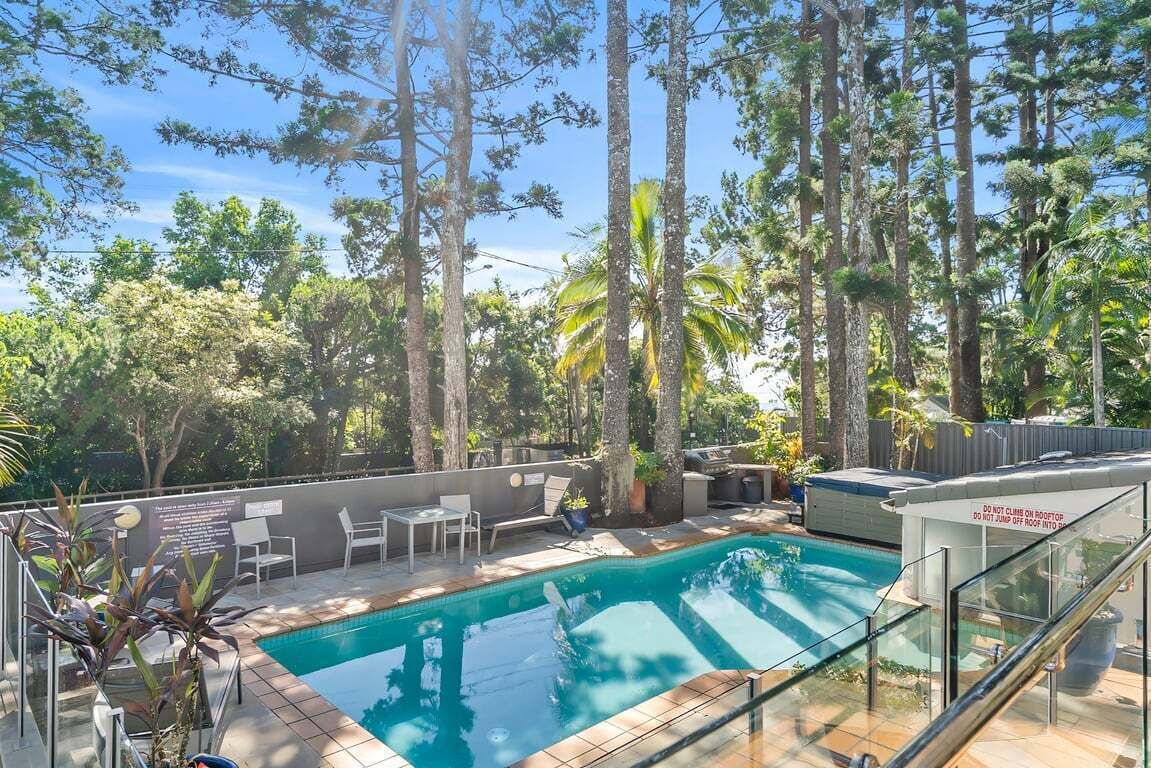 A swimming pool surrounded by trees, with a glass railing and outdoor furniture.