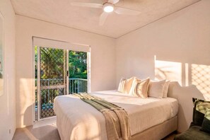 Ein Schlafzimmer mit Bett, Deckenventilator und Blick durch eine Schiebetür auf einen Außenbereich.