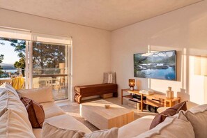 Una sala de estar moderna con sofá, mesa de centro y televisor. Hay una puerta corrediza de vidrio que da a un espacio exterior.