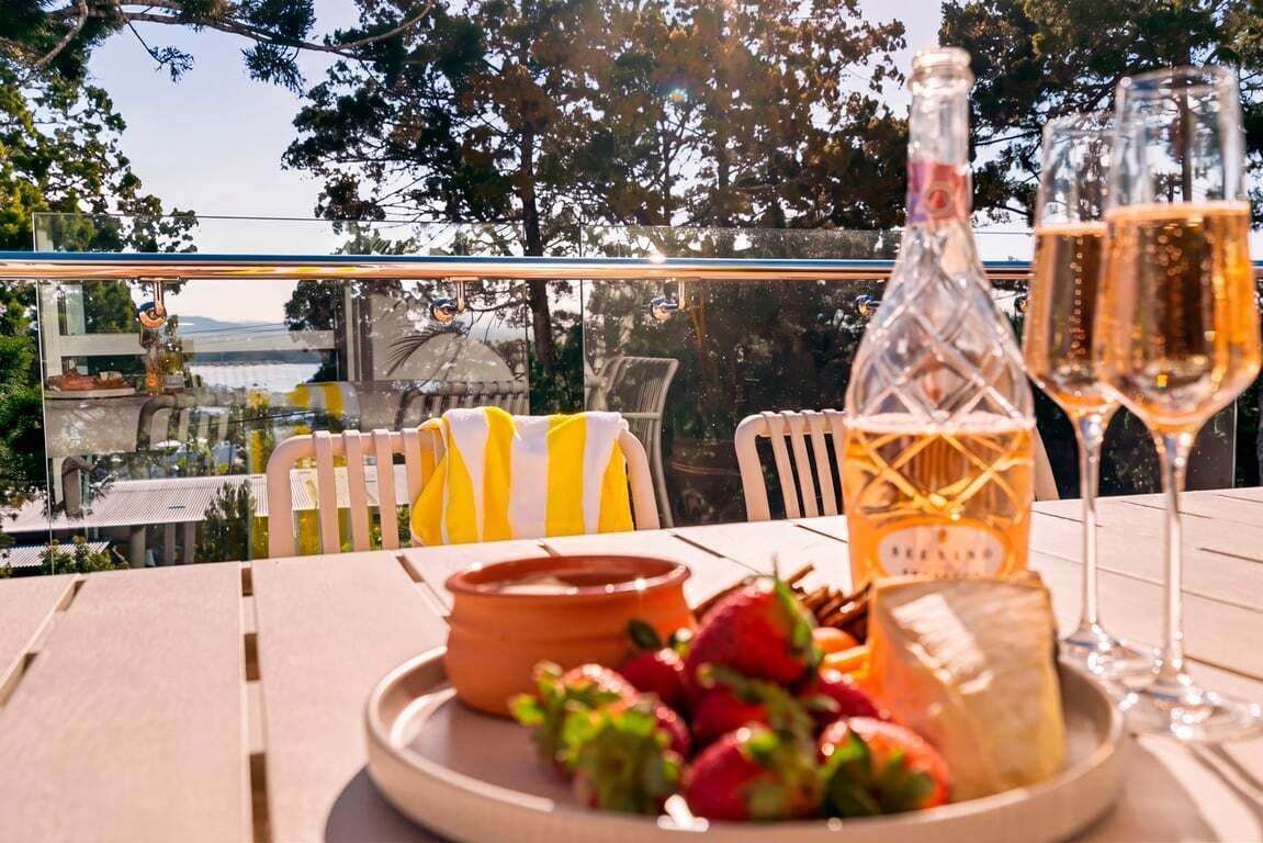 A table with a bottle of wine, two glasses of wine, a plate with strawberries, and a cheese wheel.