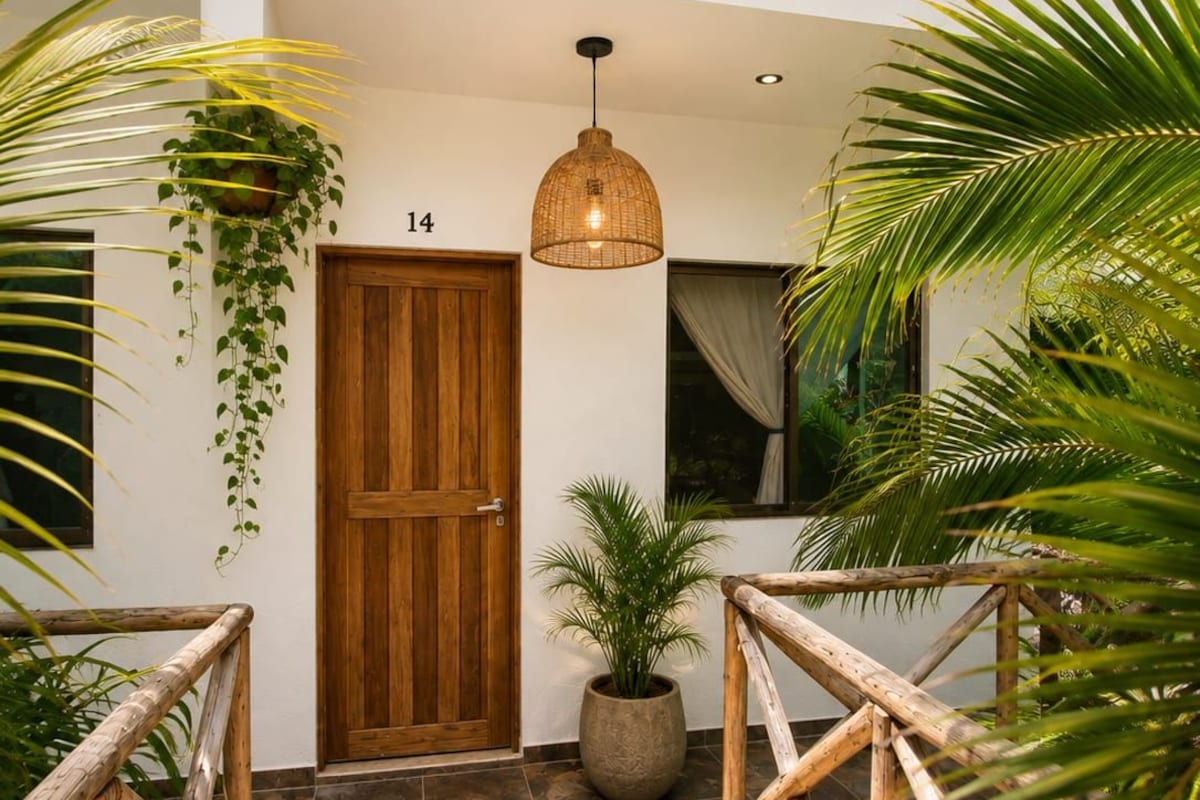 A wooden door with a number '14' above it, a hanging plant, a potted plant, and a woven light fixture.
