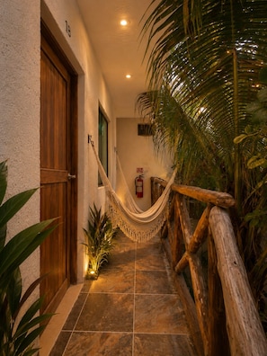 A hallway with a wooden door, a hammock, and a fire extinguisher on the wall. - Hotel Holbox Centro (Isla Holbox)