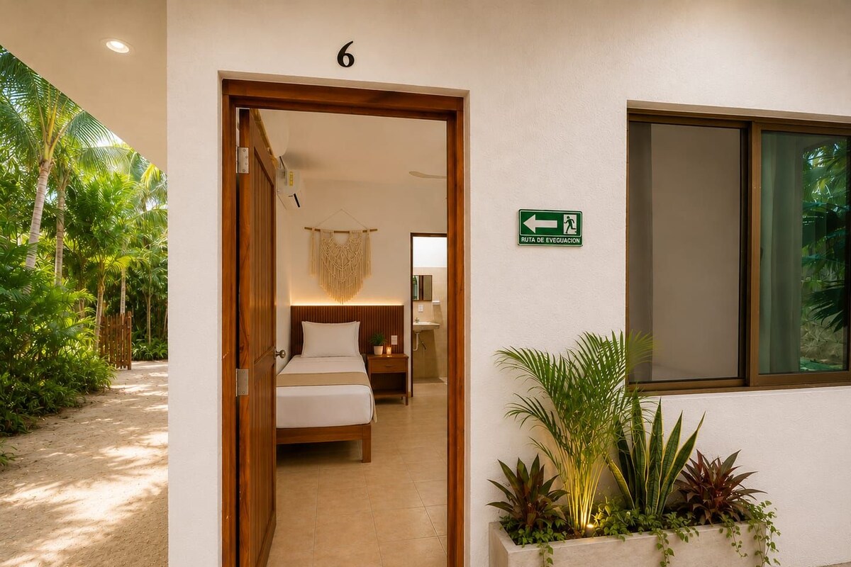 A hotel room with a bed, bedside table, and a window. There is a sign indicating an evacuation route and a number '6' on the wall.