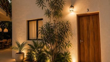 Un edificio con puerta de madera, ventana con cortina y planta en maceta.