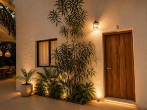 A building with a wooden door, a window with a curtain, and a potted plant. - Hotel Holbox Centro (Isla Holbox)