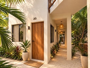 A modern house with a wooden door, number 20, and a pathway leading to a covered area with plants. - Hotel Holbox Centro (Isla Holbox)