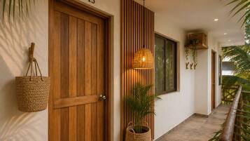 Un pasillo con una puerta de madera con el número 13, una cesta tejida colgada en la pared, una lámpara de pie tejida y una planta en maceta.