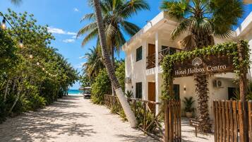 Caminho que leva a um hotel chamado 'Hotel Holbox Centro', com vista para a praia, cercado por palmeiras e uma praia de areia.