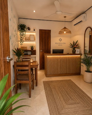 A hotel reception area with a wooden desk, a reception counter, a ceiling fan, and potted plants. - Hotel Holbox Centro (Isla Holbox)