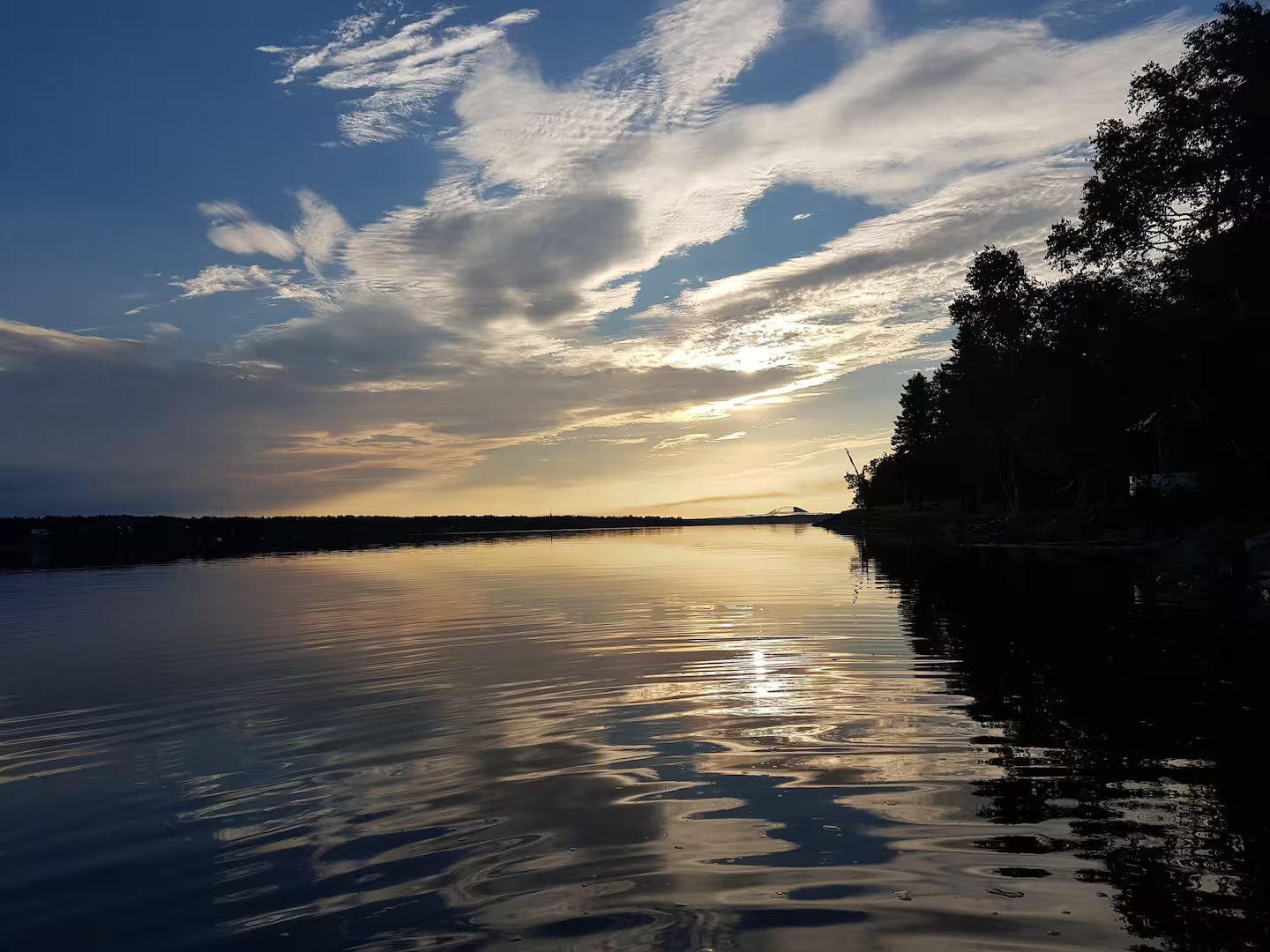 Ruhige Wasserfläche spiegelt den Himmel wider, umgeben von Bäumen und einem fernen Horizont.