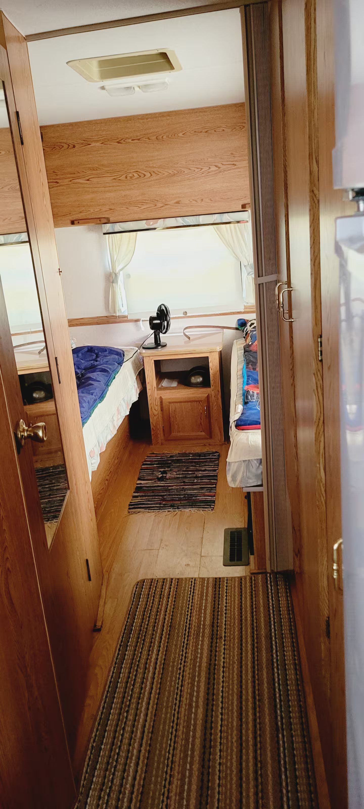 A compact, well-lit room with a bed, a small desk, and a fan.