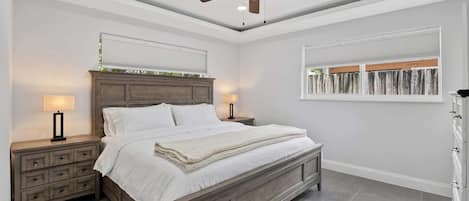 Quarto com cama, mesas de cabeceira, ventoinha no teto e janela com persianas.
