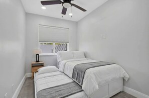 Ein Schlafzimmer mit einem Bett, einem Nachttisch, einem Deckenventilator und einem Fenster mit Jalousien.