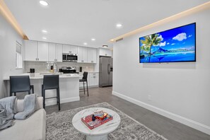 A modern kitchen with white cabinets, a central island, and a large flat-screen TV on the wall. - Coveside Hideaway 1 & Coastal Retreat (Deerfield Beach)