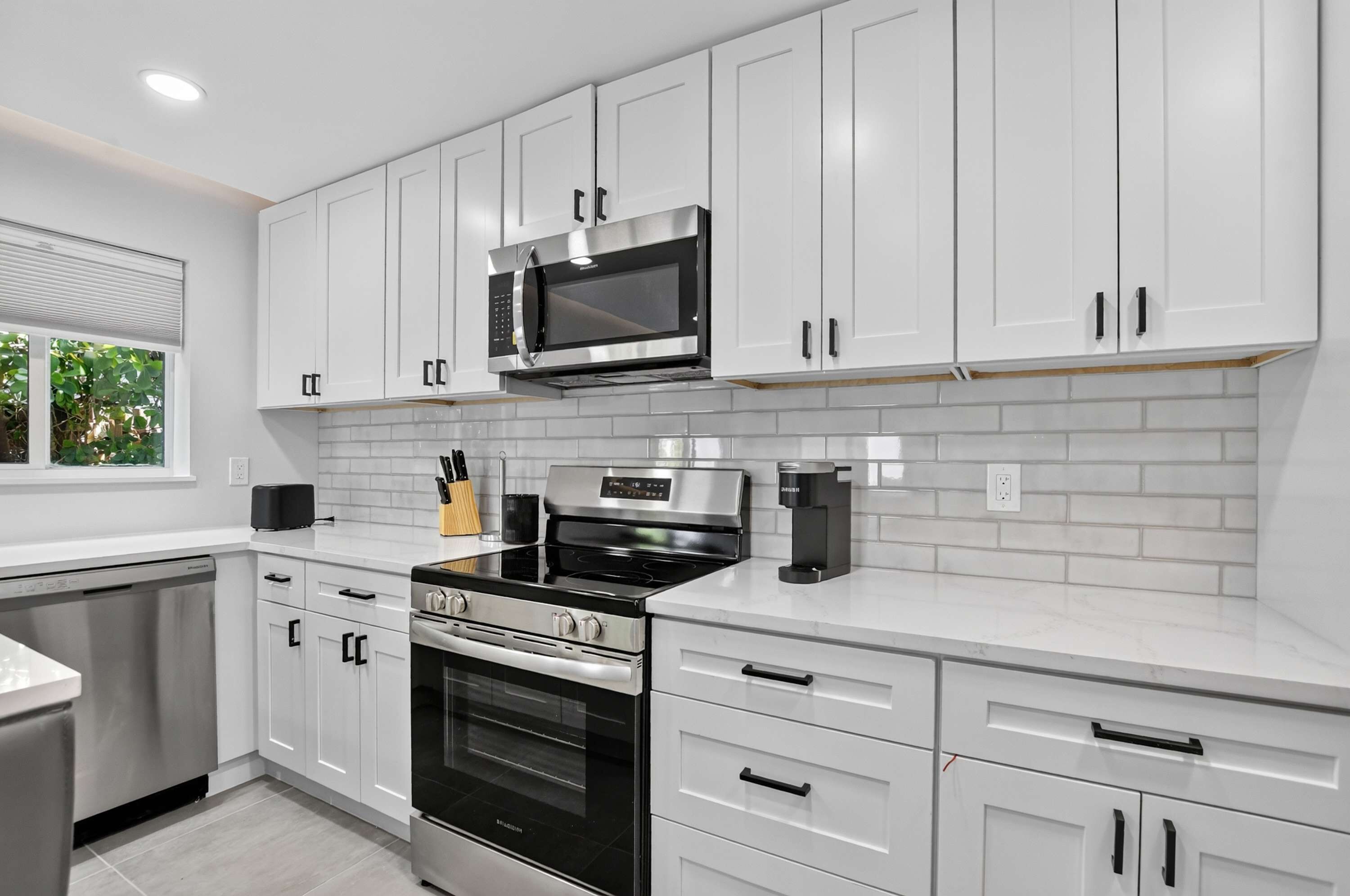 Una cocina moderna con armarios blancos, un microondas de acero inoxidable, una estufa a gas y un horno empotrado.