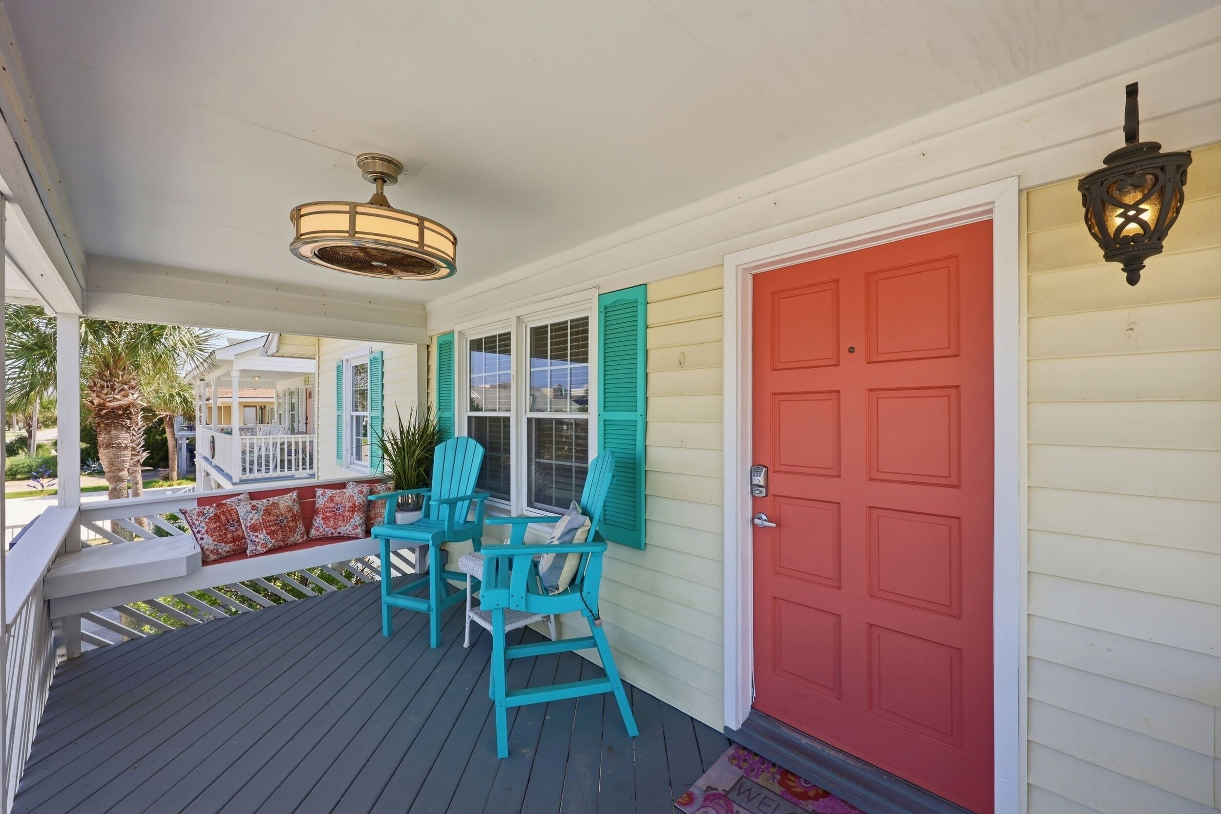 A porch with two chairs, a red door, and a hanging light fixture.