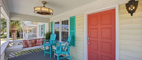 A porch with two chairs, a red door, and a hanging light fixture.