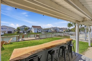 A covered outdoor area with a bar and seating, overlooking a water body and residential buildings. - Silver Sand Dollar | Upscale 6BR Escape-Hot Tub (North Myrtle Beach)