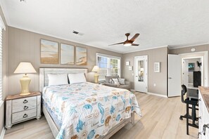 Ein Schlafzimmer mit einem Bett, Nachttischlampen, einem Deckenventilator und Kunstwerken an den Wänden.