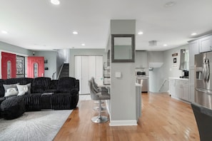 A modern kitchen with stainless steel appliances, a grey dining area with a high chair, and a staircase leading to an upper level. - Modern 4BR Retreat Spacious Living, Fireplace & Finished Basement (Matteson)