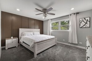 A bedroom with a bed, nightstands, a ceiling fan, a window with curtains, and a wall-mounted artwork. - Modern 4BR Retreat Spacious Living, Fireplace & Finished Basement (Matteson)