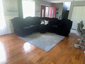 A living room with a sectional sofa, a grey rug, wooden flooring, a red door, and a staircase. - Modern 4BR Retreat Spacious Living, Fireplace & Finished Basement (Matteson)
