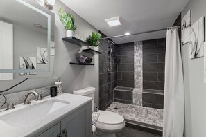 A modern bathroom with a large mirror, two sinks, a toilet, and a shower area. - Modern 4BR Retreat Spacious Living, Fireplace & Finished Basement (Matteson)