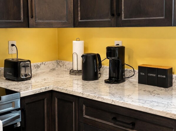 A kitchen with a marble countertop, a toaster, a coffee maker, a paper towel holder, and a set of containers labeled tea, coffee, and sugar. - Luxurious Apartment in St. John’s (St. John's)