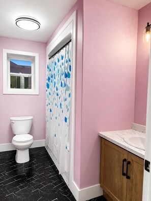A bathroom with a white toilet, a shower curtain with blue patterns, a window, and a wooden cabinet. - Luxurious Apartment in St. John’s (St. John's)