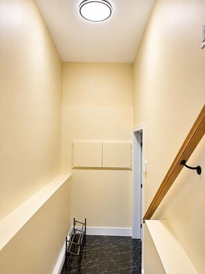 Ein schmaler Flur mit einer Holztreppe auf der rechten Seite, einer weißen Tür am Ende und einem schwarzen Fliesenboden.