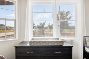 A room with a dark wooden dresser, a window with a view of a landscape, and a white curtain.