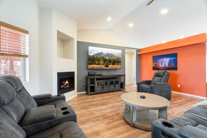 A modern living room with a fireplace, a flat-screen TV, a massage chair, and a round coffee table.