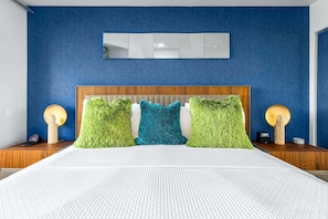 A bedroom with a large bed, a wooden headboard, and three colorful pillows. - Casa del Segundo | MCM 1BR | 2 Pools & Tennis | Palm Springs (Palm Springs)